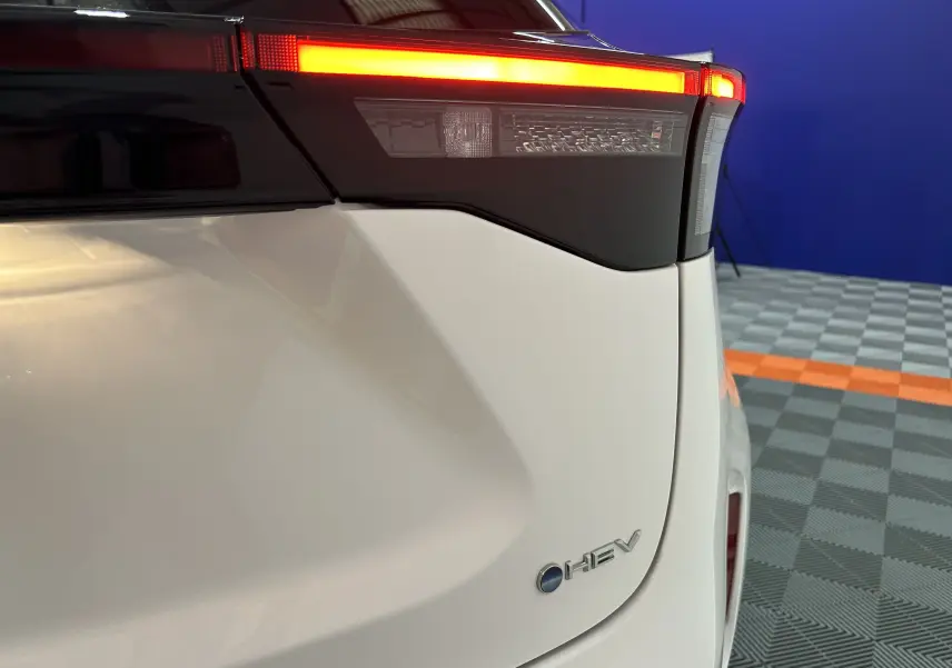 Gros plan sur le feu arrière droit allumé d'une Toyota Yaris Cross blanche hybride avec logo HEV visible.