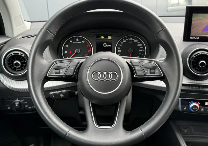 Vue rapprochée du volant noir de l'Audi Q2 35 TFSI 150 S-Tronic S-Line avec commandes intégrées et tableau de bord visible.