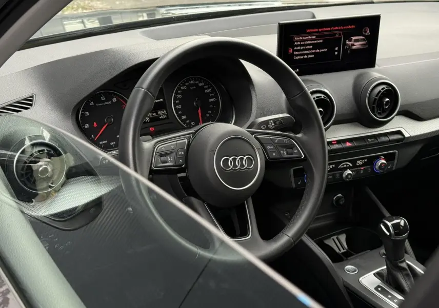 Vue intérieure de l'Audi Q2 35 TFSI 2023 montrant le volant, tableau de bord et écran central avec commandes modernes.