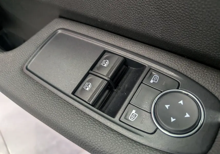 Gros plan sur les commandes des vitres électriques et réglages des rétroviseurs côté conducteur d'une Renault Clio V blanche.