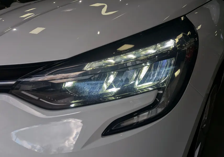 Gros plan sur le phare avant droit allumé d'une Renault Clio V Blue dCi 100 CH BUSINESS blanc glacier de 2021.