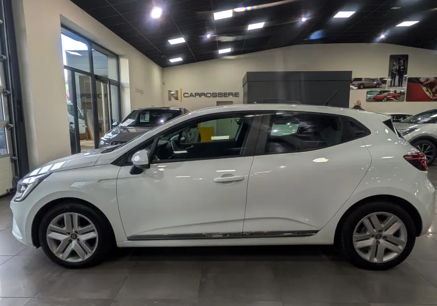 Profil latéral droit d'une Renault Clio V blanc glacier en showroom, soulignant ses jantes alliage et lignes épurées.
