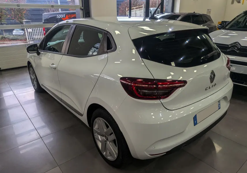 Vue 3/4 arrière droite d'une Renault Clio V Business blanche Glacier en intérieur, avec feux arrière LED distinctifs.
