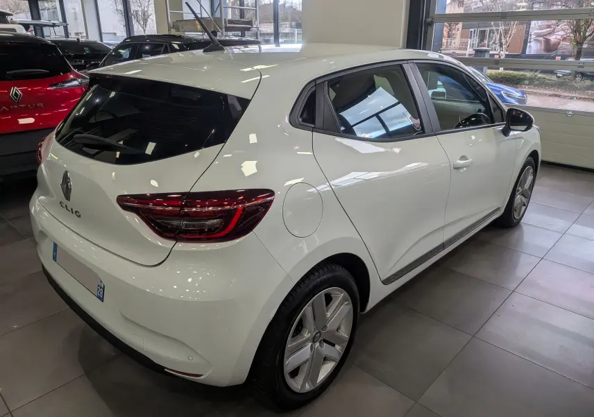 Renault Clio V Blue dCi 100 blanc glacier vue 3/4 arrière droit en intérieur avec jantes alliage et vitres teintées.