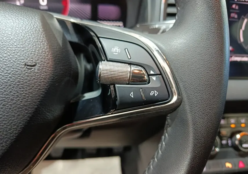 Gros plan sur les commandes multifonctions côté gauche du volant cuir noir du Skoda Karoq 2024.