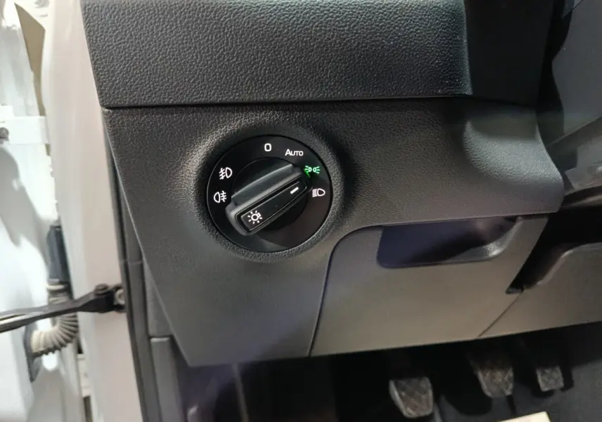 Gros plan sur le bouton de commande des phares noir dans l'habitacle gris foncé d'une Skoda Karoq 2024.