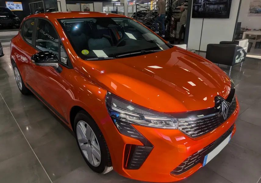 Renault Clio V Orange Valencia vue 3/4 avant droit en intérieur, avec calandre et phares LED distinctifs.