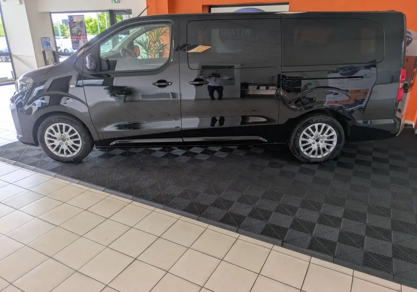 Vue de profil côté gauche d’un Peugeot Traveller noir 2026 en intérieur, avec jantes alliage et vitres teintées.