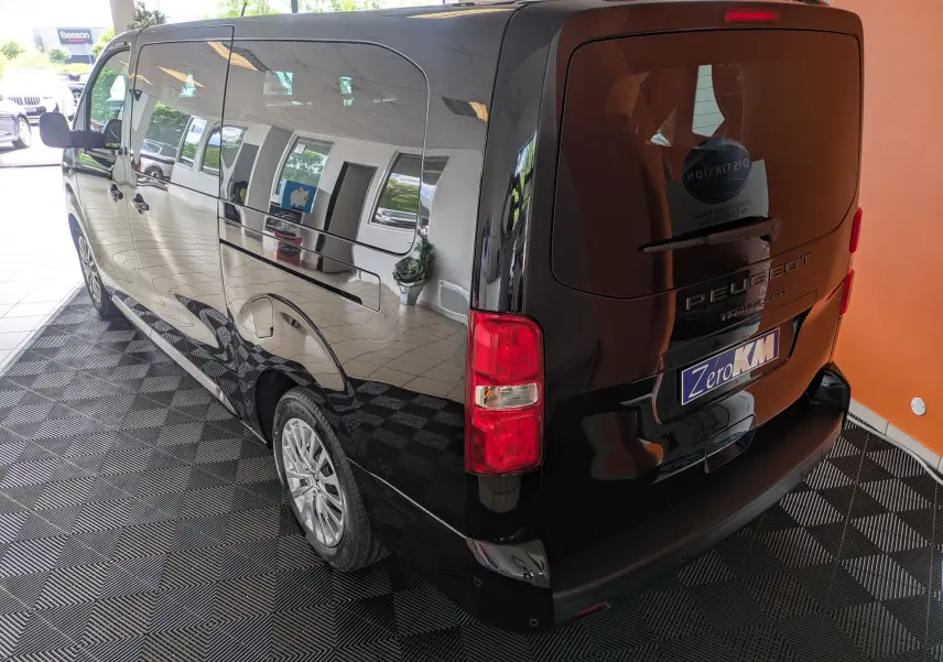 Vue 3/4 arrière gauche d'un Peugeot Traveller noir 2026, grand van avec vitres latérales teintées et feux arrière rouges.