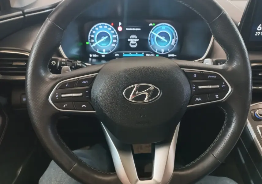 Vue intérieure centrée sur le volant cuir noir et le tableau de bord numérique du Hyundai Santa Fe hybride gris clair 2021.