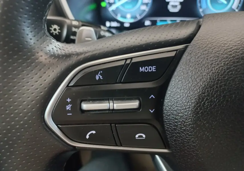 Gros plan sur les commandes noires du volant cuir du Hyundai Santa Fe hybride, avec touches mode et téléphone.