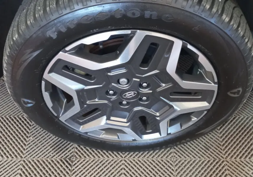 Gros plan sur la roue avant avec jante alliage gris et logo Hyundai au centre, pneu Firestone visible.
