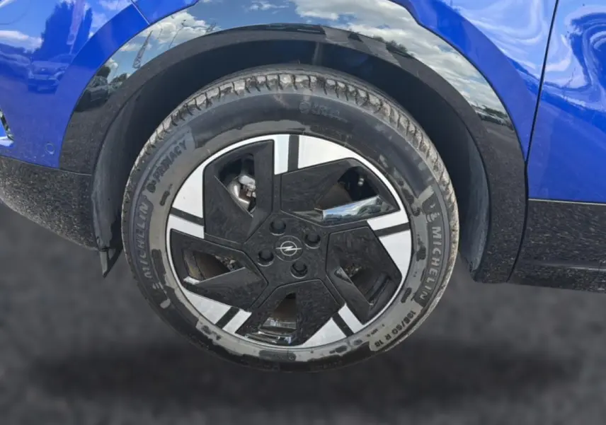 Gros plan sur la roue avant droite d’un Opel Mokka Electric 156 gs bleu, avec jante alu au design moderne bicolore.