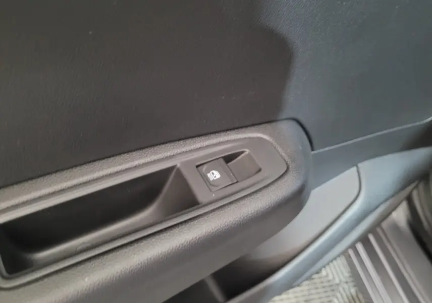 Bouton de commande de vitre sur la porte côté conducteur d'une Renault Clio gris foncé, intérieur sobre en plastique noir.