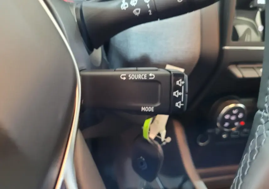 Gros plan sur la commande multimédia au volant d'une Renault Clio gris foncé, intérieur noir avec coutures grises.