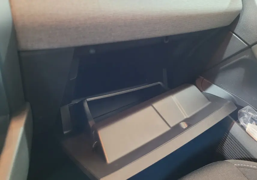 Gros plan sur la boîte à gants ouverte côté passager de la Renault Clio gris foncé, intérieur tissu sombre.