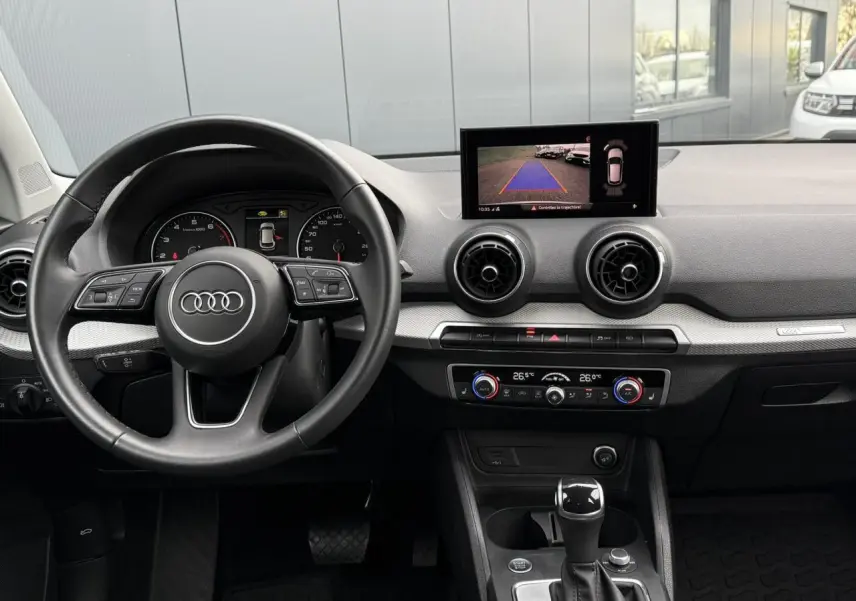 Vue intérieure de l'Audi Q2 35 TFSI S-Line 2023 montrant le volant, l'écran de caméra de recul et la console centrale noire.