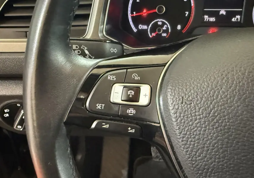 Gros plan sur le volant cuir noir du Volkswagen T-Roc 2020, montrant les commandes du régulateur adaptatif et tableau de bord numérique.