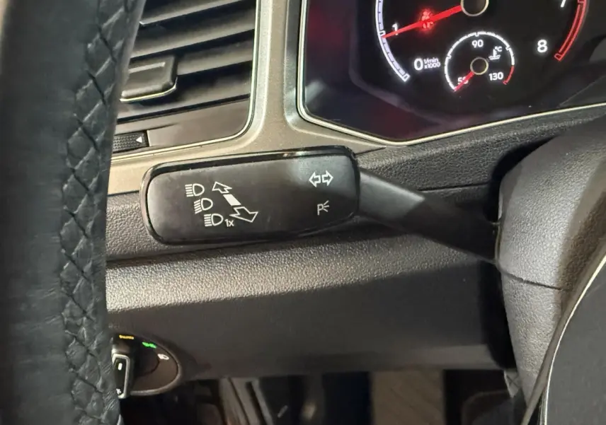 Gros plan sur la manette de clignotants à gauche du volant cuir du Volkswagen T-Roc noir, tableau de bord partiellement visible.