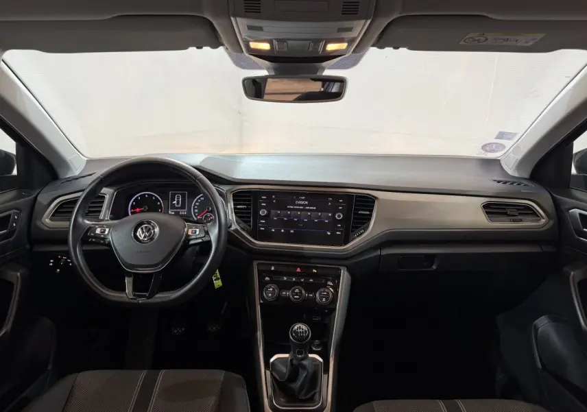 Intérieur avant du Volkswagen T-Roc noir 2020, vue frontale sur tableau de bord, volant cuir et écran tactile central.