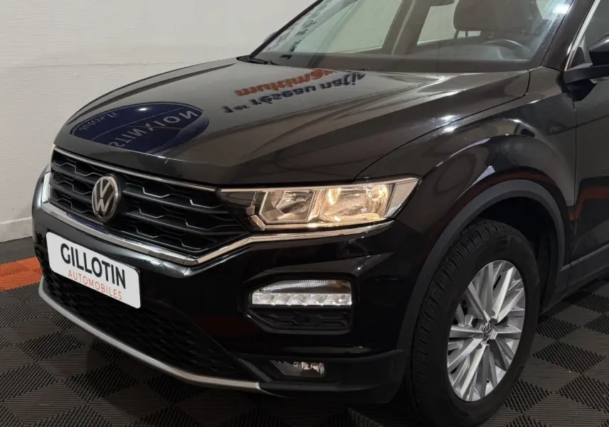 Vue 3/4 avant droit d'un Volkswagen T-Roc noir avec phares allumés et jantes alliage visibles.