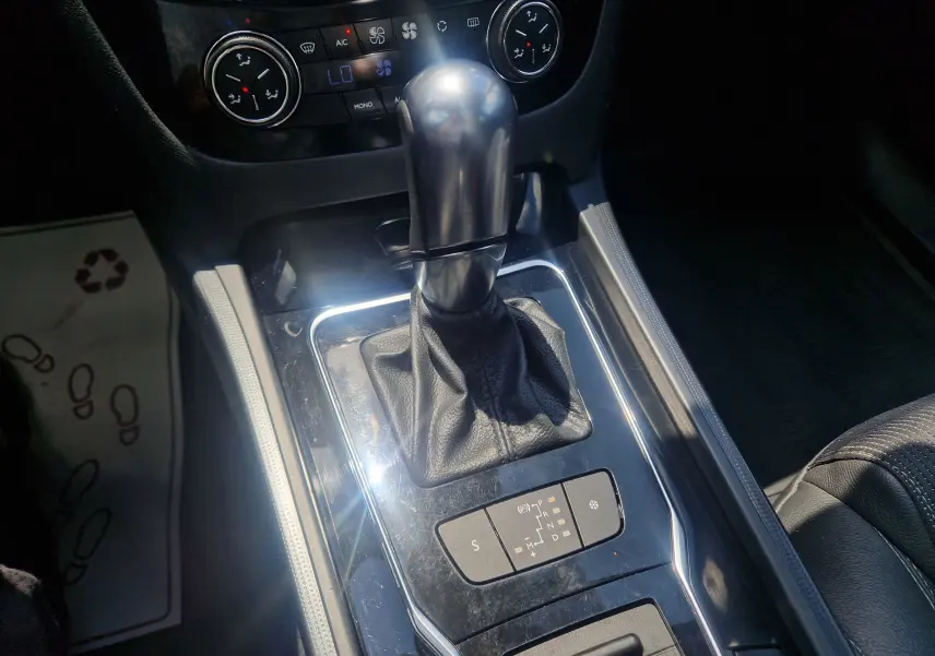 Gros plan sur le levier de vitesse automatique d'une Peugeot 508 SW gris Shark, avec commandes de climatisation visibles en arrière-plan.