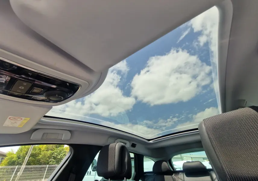 Vue intérieure du toit panoramique ouvrant du Peugeot 508 SW gris Shark, avec ciel bleu et nuages visibles.