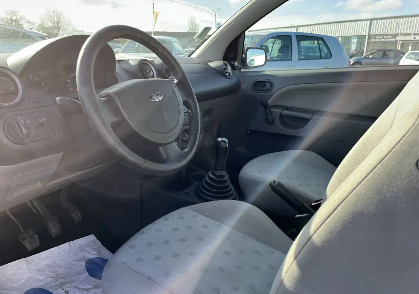 Intérieur de la Ford Fiesta 2003, vue côté conducteur, volant avec logo Ford et levier de vitesse manuel visible.