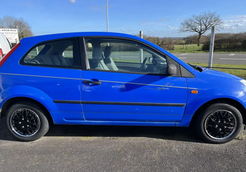 Profil côté gauche d'une Ford Fiesta 3 portes bleu vif de 2003 avec jantes noires et décoration latérale grise.