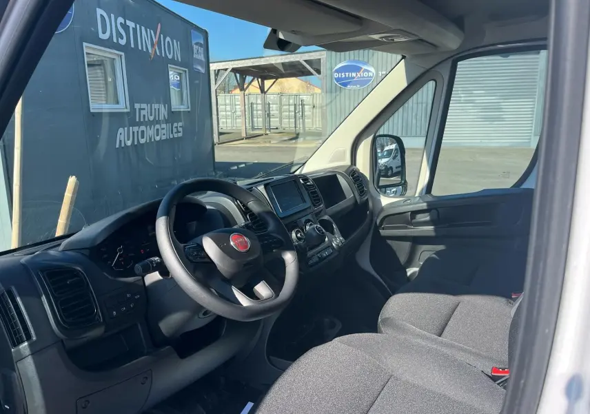 Vue intérieure côté conducteur du Fiat Ducato Fourgon blanc 2023, tableau de bord et sièges gris visibles.