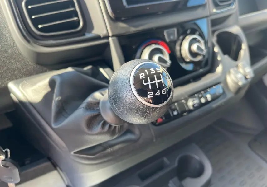 Gros plan sur le levier de vitesses manuel noir du Fiat Ducato Fourgon 2023, avec tableau de bord et commandes clim visibles.