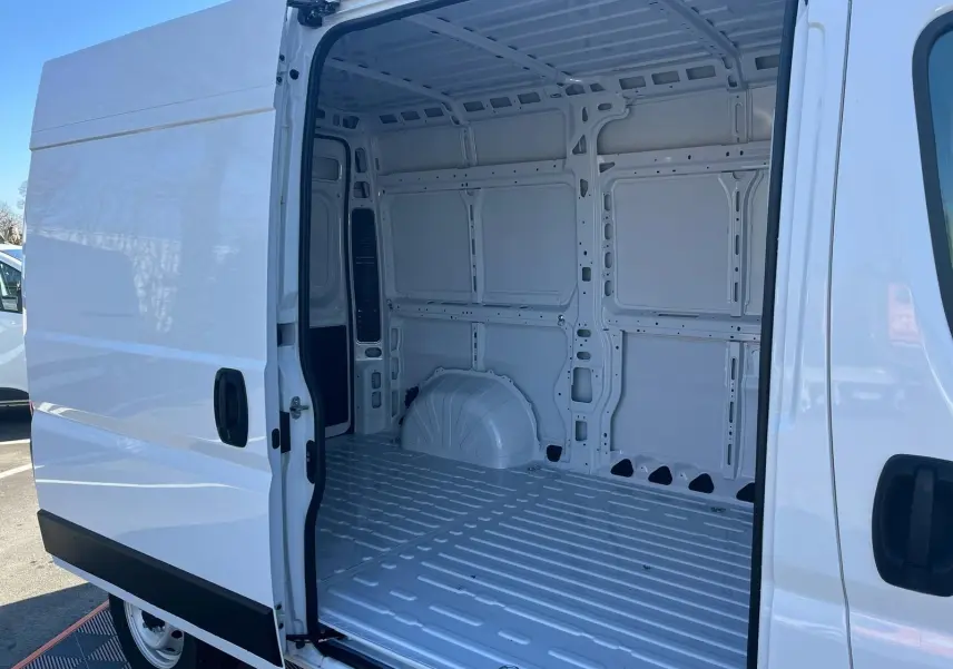 Vue latérale gauche du fourgon blanc FIAT Ducato 2023 avec porte coulissante ouverte montrant l’intérieur vide et métallique.