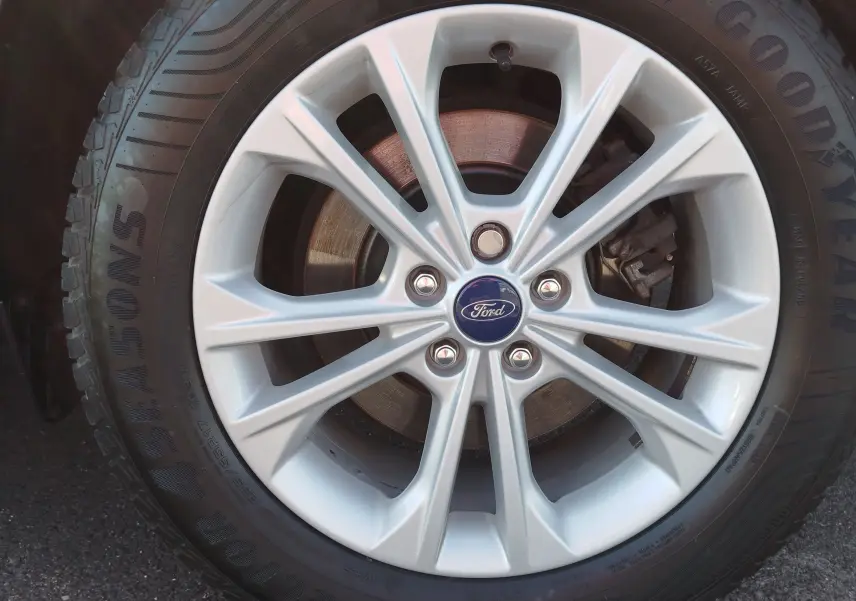 Gros plan sur la jante alliage argentée d'un Ford Kuga gris clair, avec logo Ford au centre et pneu Goodyear visible.