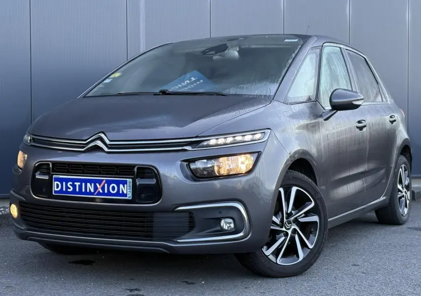Citroën C4 Picasso gris Platinium vue 3/4 avant droit avec feux allumés et jantes alliage bi-ton.