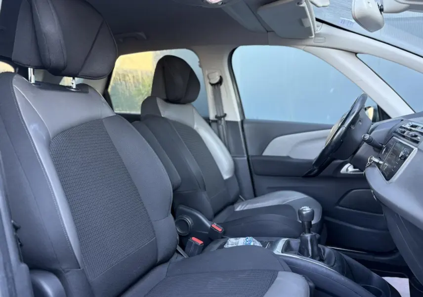 Vue intérieure côté conducteur de la Citroën C4 Picasso 2017, sièges tissu noir et cuir gris, volant cuir et levier de vitesses manuel.