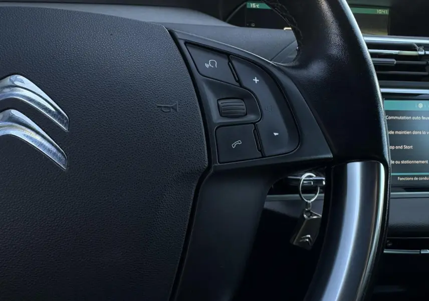 Gros plan sur le volant cuir noir de la Citroën C4 Picasso 2017 avec commandes intégrées et clé insérée au contact.