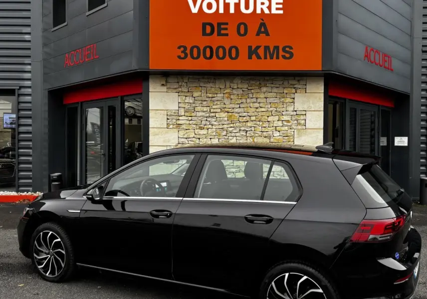 Volkswagen Golf 1.5 ETSI noire vue de profil côté gauche devant un bâtiment avec panneau orange "Votre nouvelle voiture"