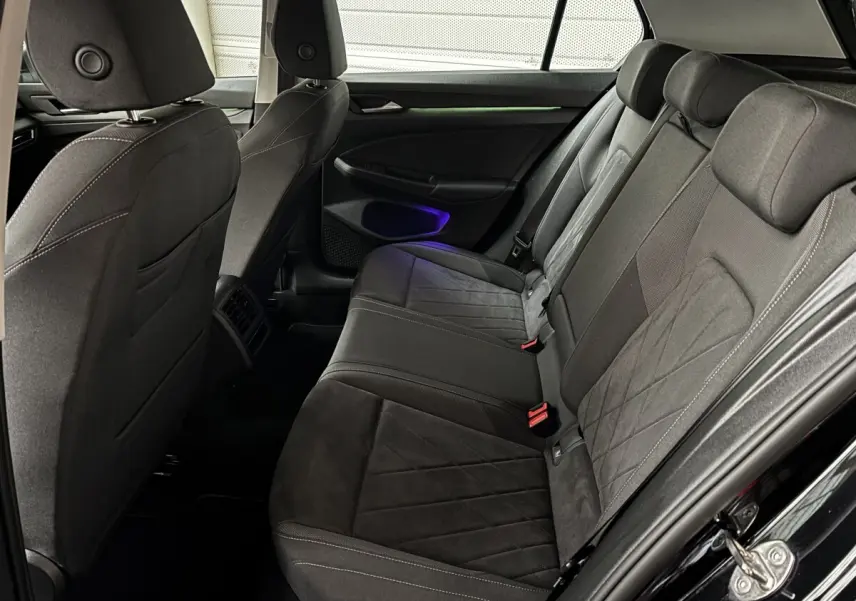 Vue latérale droite de l'arrière de la Volkswagen Golf noire 2024, montrant les sièges en tissu et alcantara avec éclairage d'ambiance violet.