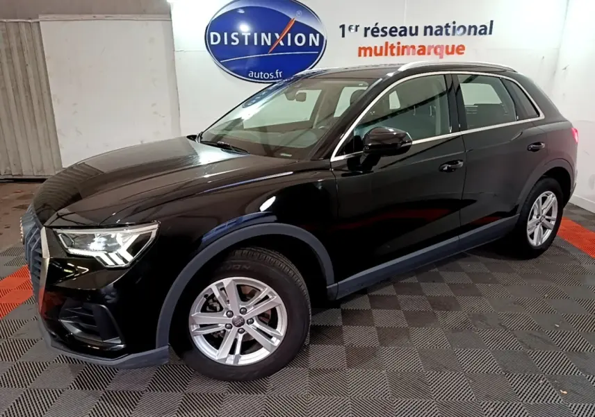 Audi Q3 noir vue 3/4 avant droit dans un showroom avec jantes argentées et phares allumés.