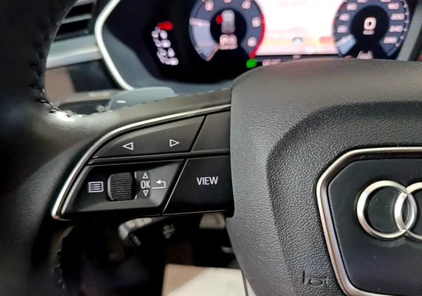 Gros plan sur le volant noir d'Audi Q3 35 TDI 150 S tronic Business Line avec commandes multifonctions et tableau de bord numérique.