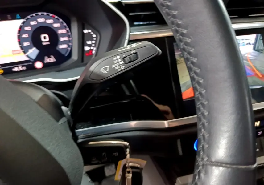 Vue intérieure rapprochée côté gauche du volant cuir d’un Audi Q3 35 TDI 150 S tronic avec tableau de bord numérique et caméra de recul.