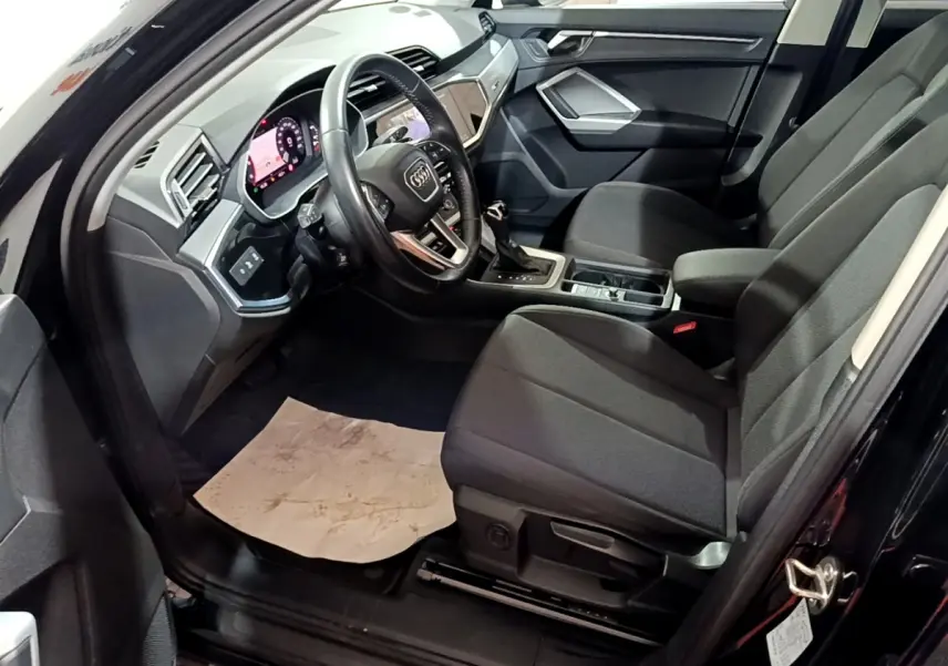 Intérieur côté conducteur de l’Audi Q3 noir 2020, montrant sièges tissu noirs et tableau de bord digital moderne.