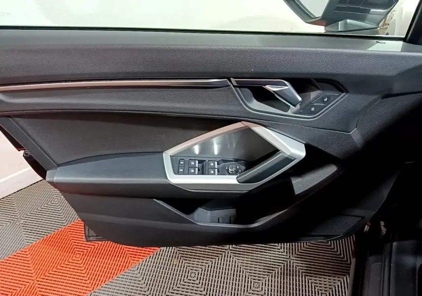Vue rapprochée de la porte côté conducteur noire de l'Audi Q3 2020 avec commandes de vitres et rétroviseurs intégrées.