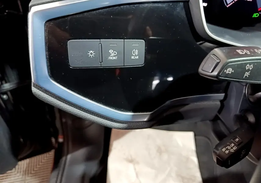 Détail du tableau de bord noir de l'Audi Q3 35 TDI 2020 montrant les commandes d'éclairage avant et arrière.