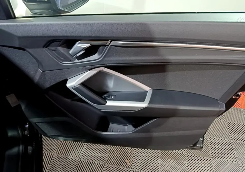 Détail de la porte côté gauche de l'Audi Q3 35 TDI 150 S Tronic Business Line noire avec poignée argentée et commandes de vitre.