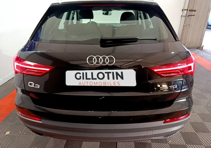 Vue arrière d'un Audi Q3 noir 35 TDI avec feux LED allumés et logo Audi visible sur un sol à damier.