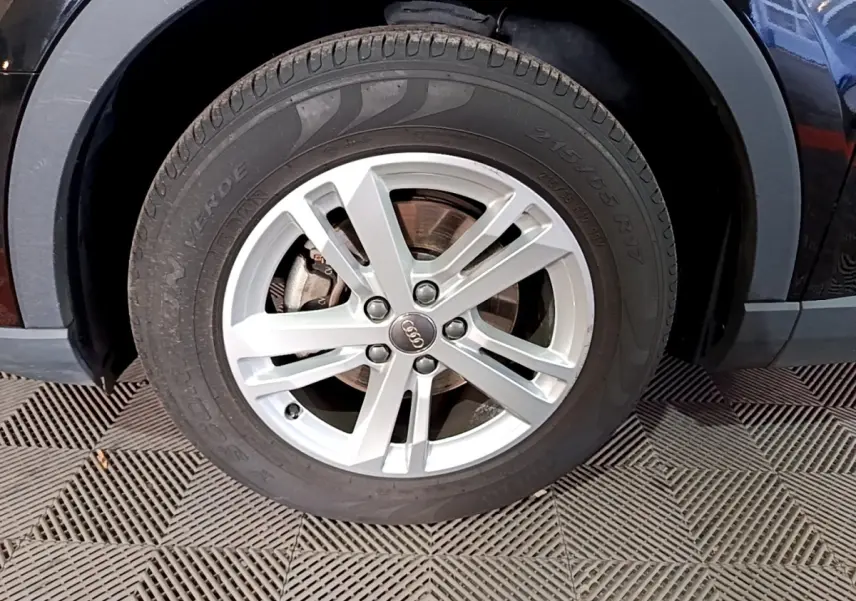 Gros plan sur la roue avant gauche noire de l'Audi Q3 35 TDI 150 S tronic Business Line avec jante argentée à 5 branches.