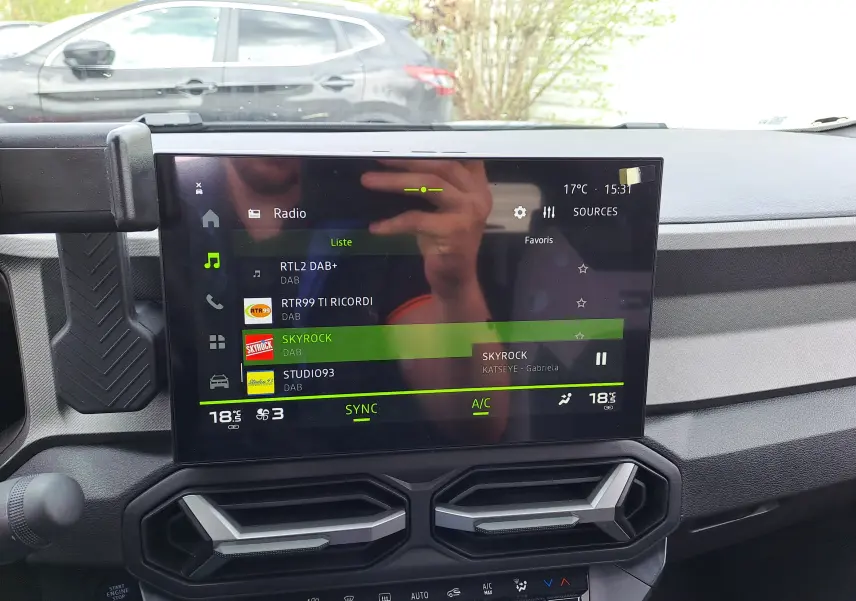 Intérieur du Dacia Bigster 2026, vue sur l'écran tactile central affichant la radio, avec tableau de bord gris et aérateurs hexagonaux.