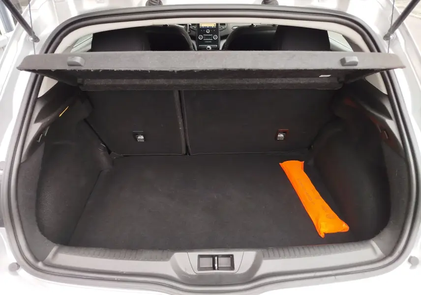 Coffre ouvert vu de l'arrière d'une Renault Mégane gris titanium, avec un triangle de signalisation orange posé à droite.