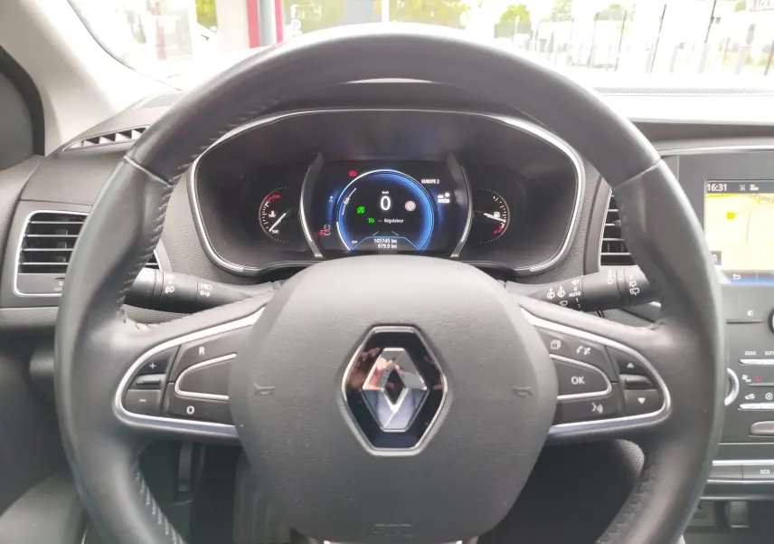 Vue intérieure centrée sur le volant Renault et le tableau de bord numérique de la Mégane gris titanium de 2018.